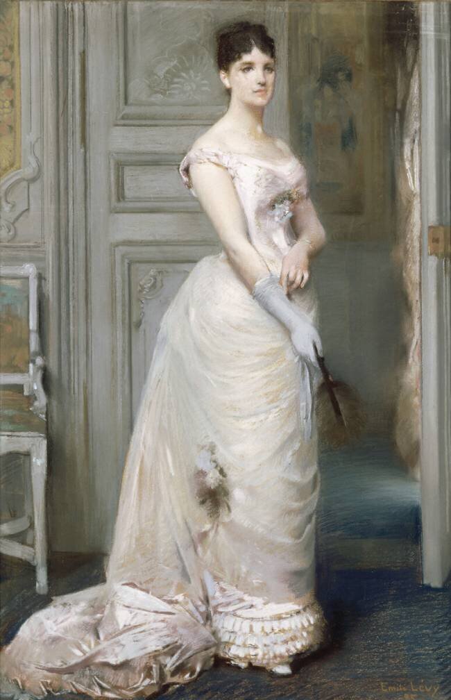 Jeune femme debout vêtue d'une robe de soirée rose et enfilant un gant Emile Levy