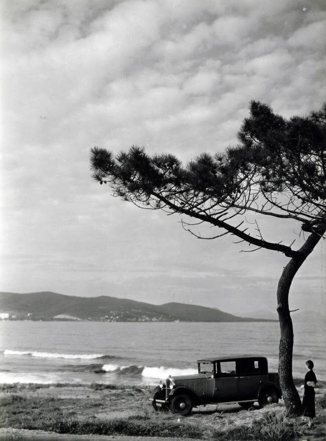 Femme contemplant le paysage vers une Citroën C6 stationnée sur un chemin vers "La petite Corse" en face de Saint-Tropez Archives Terre Blanche
