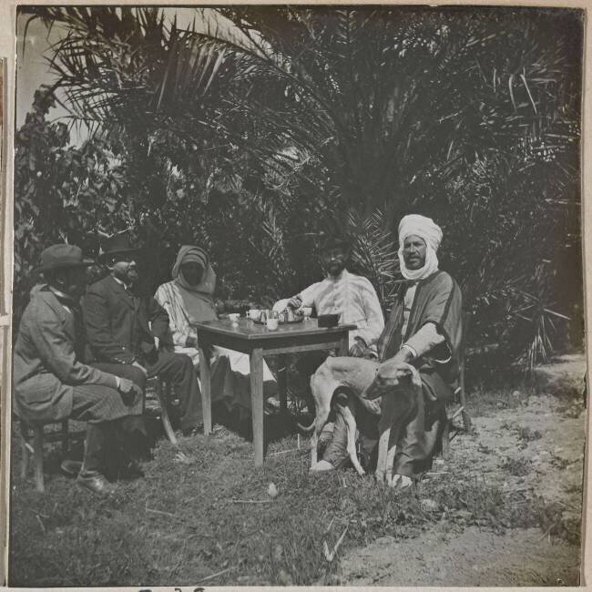Voyage en Algérie : groupe d'hommes assis autour d'une table dans un jardin à Sidi-Okba Henri Evenepoel
