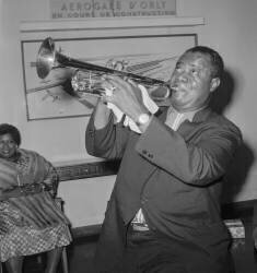 Louis Armstrong playing the trompet arriving at Orly airport, Paris (Rue des Archives) - Muzeo.com