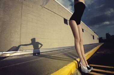 Femme en maillot de bain une pièce et chaussures à talons hauts debout contre une bordure de trottoir (anonyme) - Muzeo.com