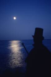 Homme de dos en chapeau haut de forme cap et canne devant la mer éclairée par la lune (Philippe Abergel) - Muzeo.com