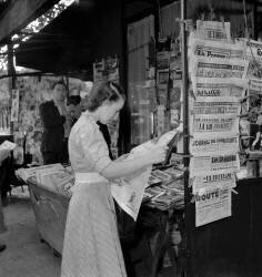 Jeune femme lisant à un kiosque à journaux, Paris, Août 1949 (Rue des Archives) - Muzeo.com