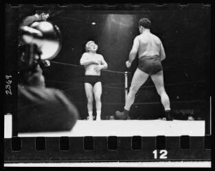 A wrestler strides toward Gorgeous George who stands near a corner of the ring with his hands on his chest where he had received a blow in the previous maneuver in the wrestling match (Stanley Kubrick) - Muzeo.com