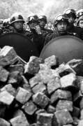 Des membres de la police anti-émeute française avec un casque et une chemise derrière un tas de pavés pendant une manifestation à Paris en mai 1968 (Rue des Archives) - Muzeo.com