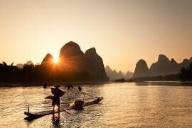 Chine, Guangxi Zhuangzu Zizhiqu, Yangshuo, pêcheur de cormorant sur la rivière Li au coucher du soleil, les montagnes karstiques en arrière-plan (Luigi Vaccarella) - Muzeo.com