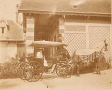Jeune femme assise dans une voiture à cheval devant une maison (anonymous) - Muzeo.com